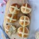 Maple Hot Cross Buns on a wooden board with a piece torn off one bun and butter spread on it - Pure Maple