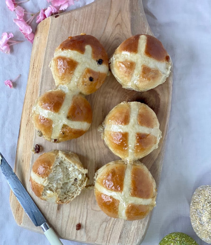 Maple Hot Cross Buns on a wooden board with a piece torn off one bun and butter spread on it - Pure Maple