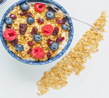 Bowl of Pure Maple Granola with added fruits, blueberries, raspberries + line of granola on table