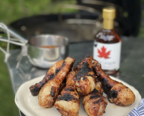 Cooked Chicken Drumsticks on plate with pot of maple syrup in background