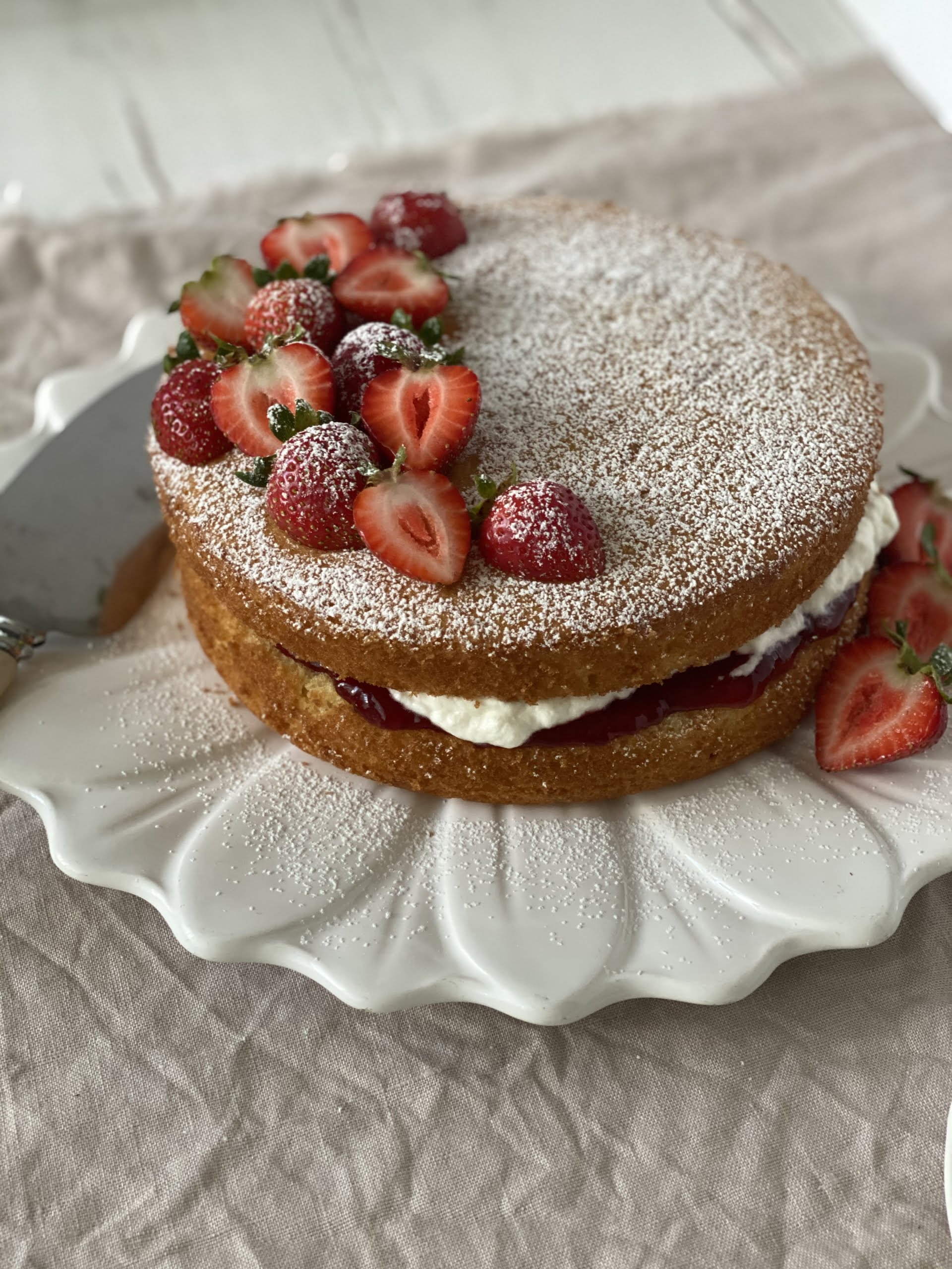 Victoria sponge cake, angle shot of cake on cake plate, decorated with strawberries and with serving knife
