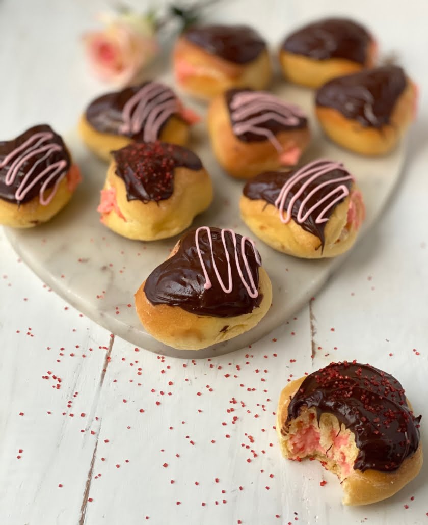 Pink cream filled chocolate covered doughnuts with a bite taken out of one - Pure Maple