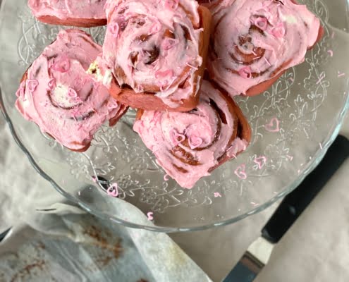 Pink Cinnamon Rolls on platter with cream covered spatula resting on tin below
