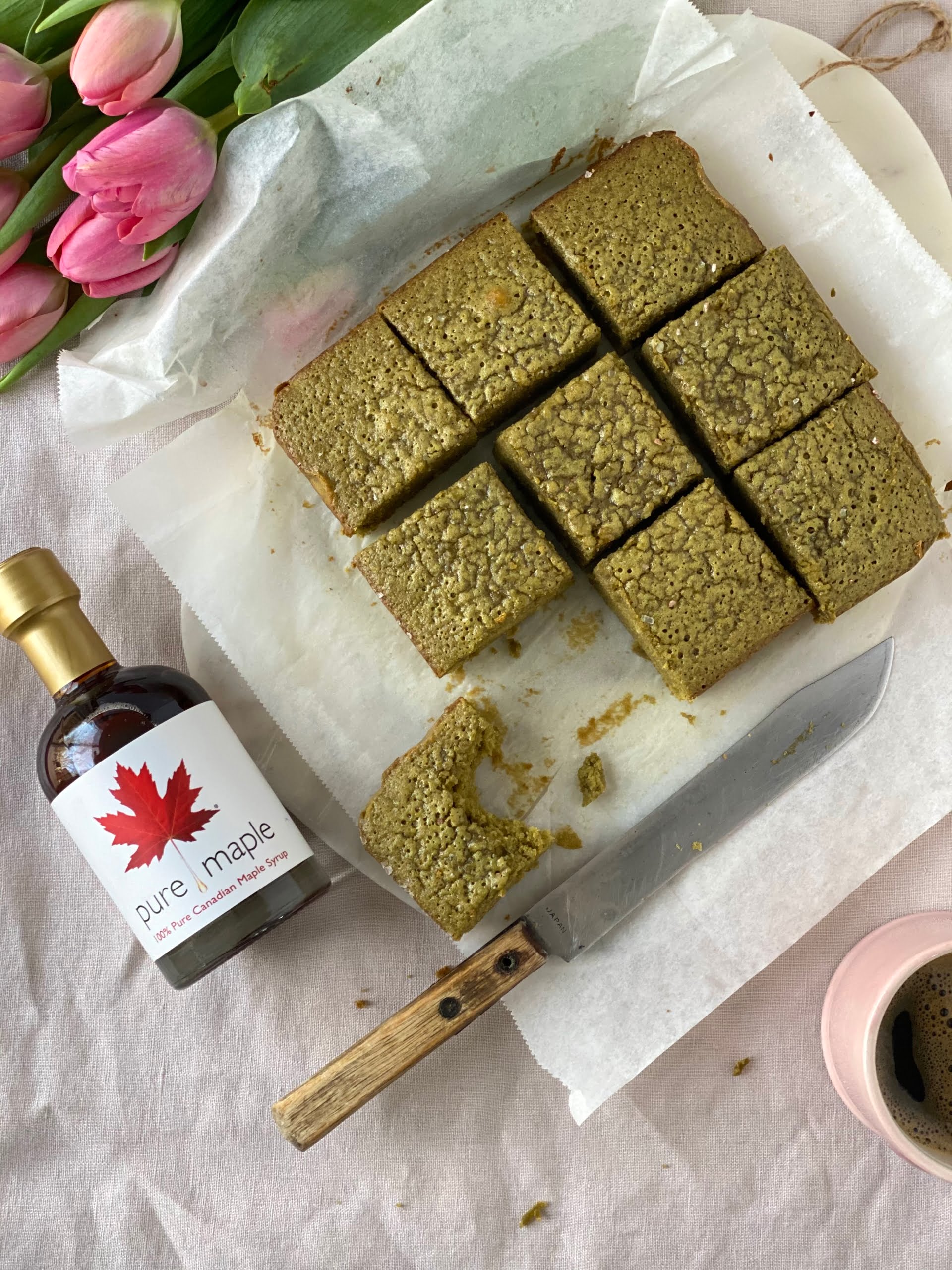 Salted Matcha Brownies with a bite taken from one and maple syrup bottle to the left - Pure Maple