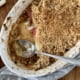 Maple rhubarb and apple crumble in an oval shallow baking dish with a couple servings removed and a large spoon to the side - Pure Maple