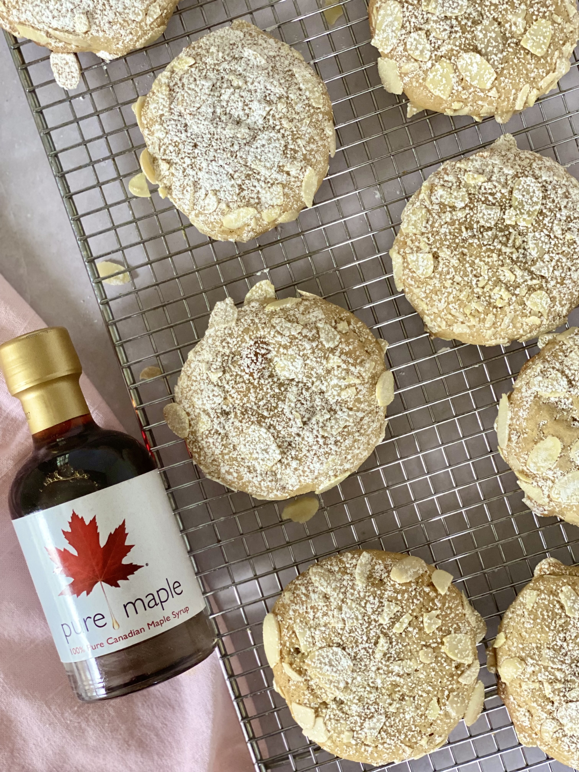 Almond cookies on a wire rack with a maple syrup at the side