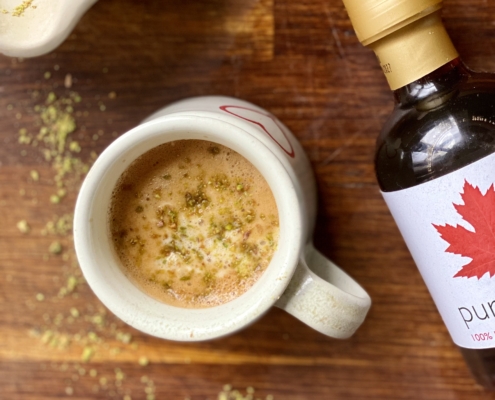 Maple pistashio coffee topped with chrushed pistachios and pure maple syrup bottle to the side